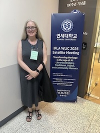 Jennifer Brannock stands in front of a banner for the IFLA conference in Korea.