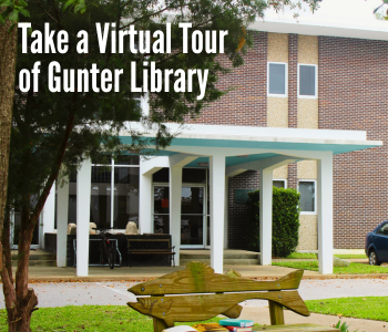 The image shows the entrance of a brick library building with a white covered walkway supported by columns. Trees frame the scene, and a fish-shaped bench sits on the lawn in the foreground. Large white text in the upper left reads, Take a Virtual Tour of Gunter Library. The setting is bright and landscaped with grass, shrubs, and a paved walkway leading to the entrance.