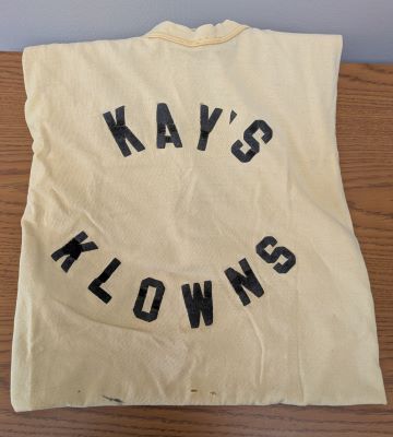 an aged yellow T-shirt with bold black lettering in the center, writing out Kay’s Klowns
